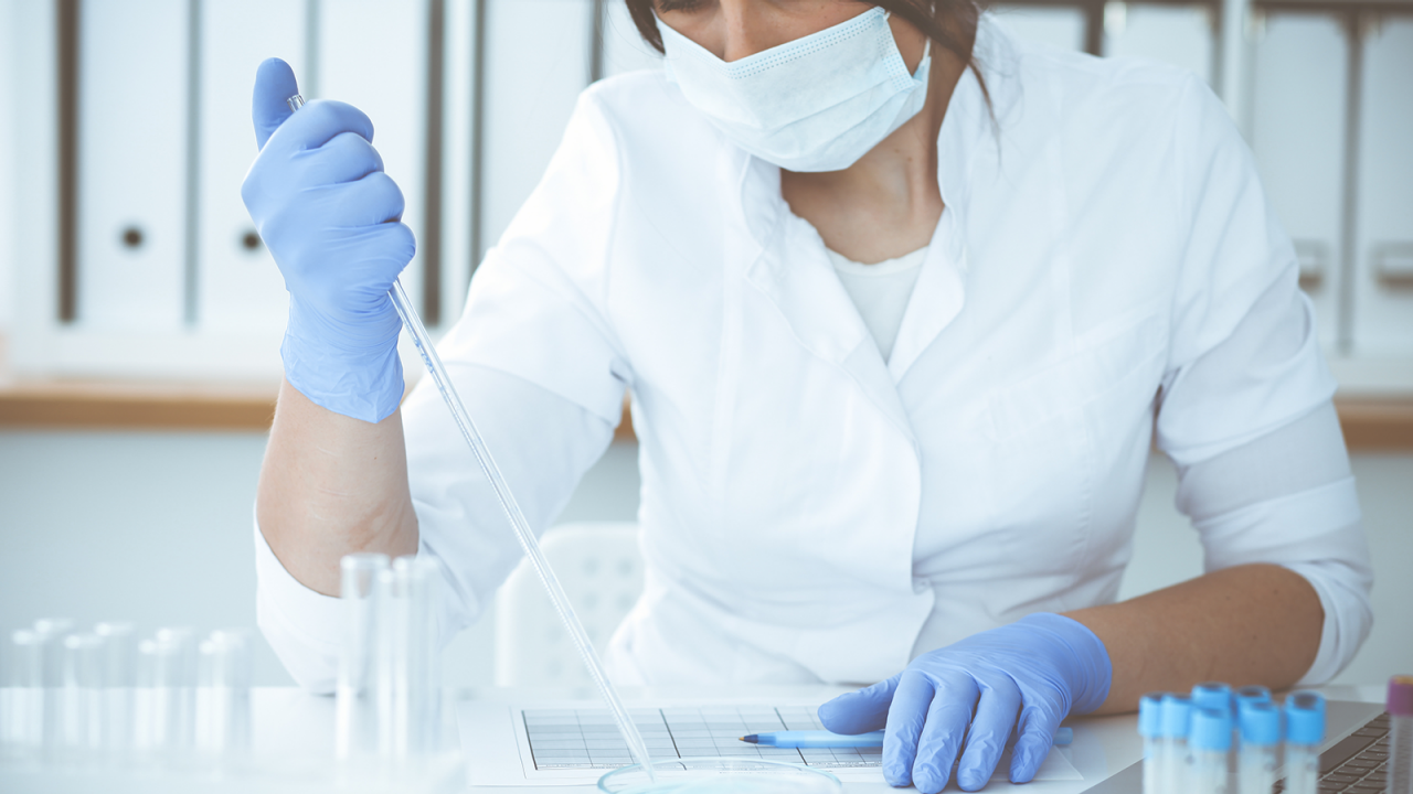 Female scientist in protective equipment designing and carrying out an experiment with reagents in a laboratory.